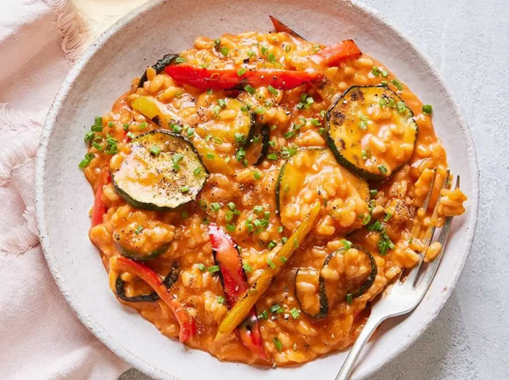 A bowl of creamy risotto with colorful bell peppers and zucchini